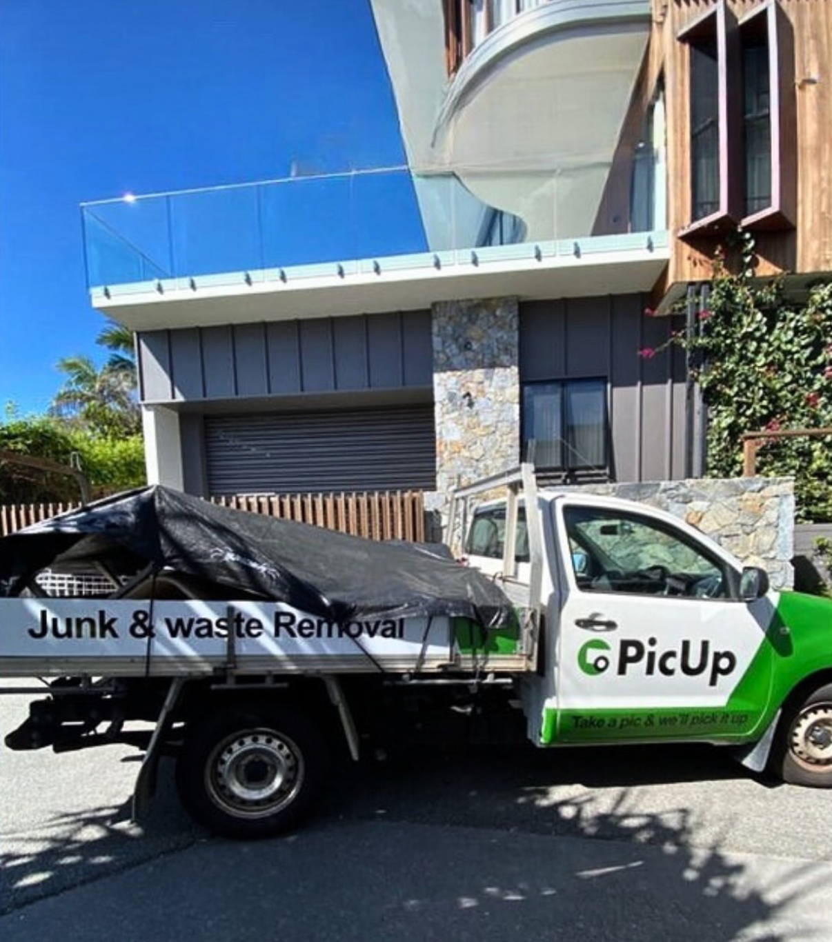 A branded PicUp junk and waste removal ute loaded with a tarped junk load outside a Sydney home